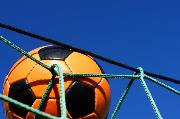 Foto vista de ángulo bajo de una pelota de fútbol en el poste de la portería contra un cielo azul claro