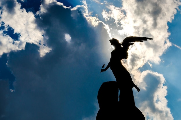 Vista de bajo ángulo de la silueta de la estatua del ángel contra el cielo nublado