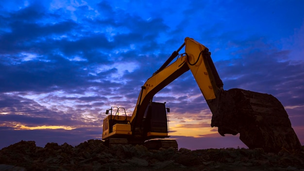 Vista de ángulo bajo de la silueta de la excavadora que trabaja para nivelar la tierra en el sitio de construcción al atardecer