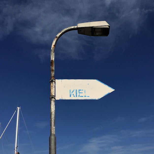 Foto vista de ángulo bajo del símbolo de la flecha con texto en la luz de la calle contra el cielo azul