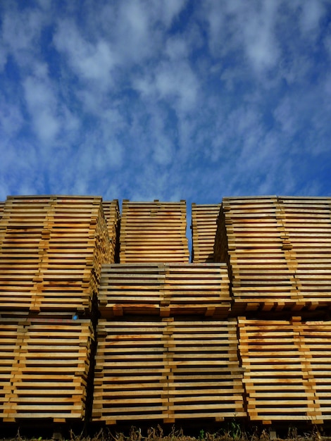 Vista de ángulo bajo de las tablas en la industria maderera contra un cielo azul nublado