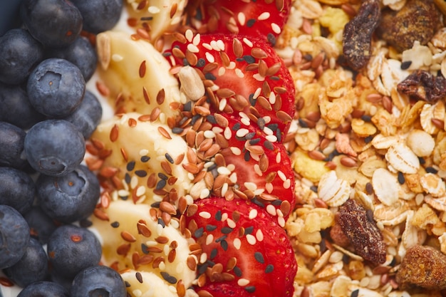 Vista anterior de cerca del delicioso postre de granola decorado con frutas y bayas con semillas de sésamo, concepto de desayuno saludable