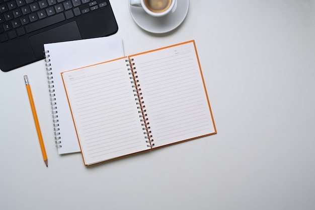 Vista anterior del cuaderno vacío, lápiz, taza de café y espacio de copia sobre fondo blanco.