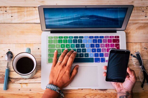 Vista anterior de la estación de trabajo de escritorio con manos de mujer que conectan el teléfono a la computadora portátil para comenzar el trabajo de trabajo inteligente moderno en línea - concepto de personas que trabajan con tecnología en el escritorio de la oficina