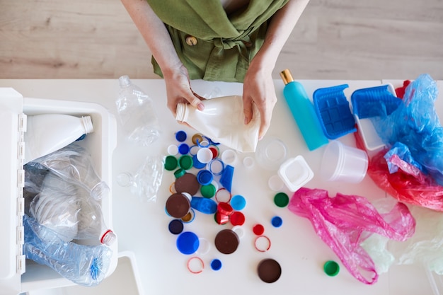 Vista anterior de irreconocible joven clasificando residuos plásticos en casa antes de reciclar