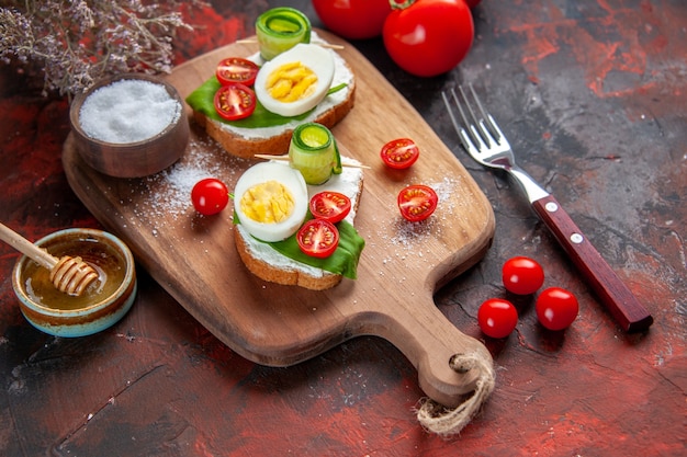 Vista anterior sabrosos sándwiches de huevo con tomates rojos sobre tabla de cortar fondo rojo oscuro almuerzo sándwich comida comida bocadillo tostadas pan hamburguesa