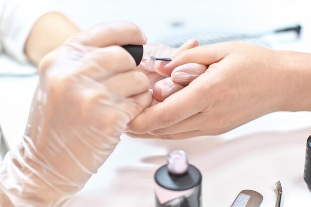 vista aproximada da manicure trabalhando no salão de beleza esteticista aplicando esmalte de gel nas unhas femininas tratamento profissional de cuidados de beleza