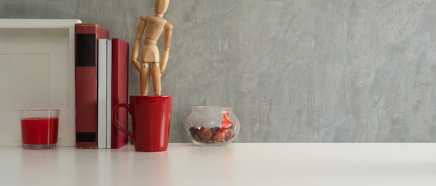 Vista aproximada da mesa de trabalho com livros, copo vermelho, moldura simulada e espaço de cópia no escritório doméstico