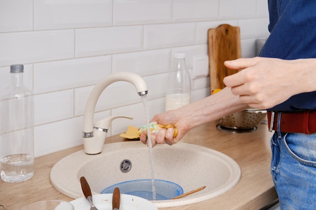 Vista aproximada das mãos masculinas lavando os pratos depois de cozinhar em casa