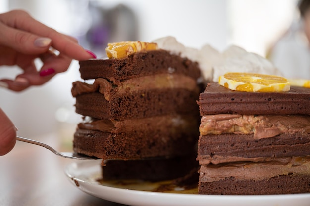 Vista aproximada de mãos femininas servindo uma fatia de delicioso bolo vegano de chocolate laranja de uma sobremesa inteira