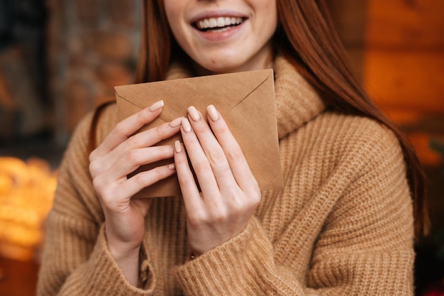 Vista aproximada de uma jovem ruiva sorridente segurando nas mãos um envelope de papel na frente dela