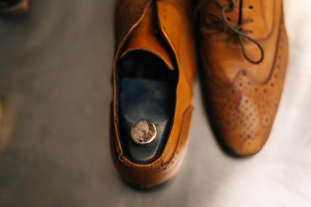 Vista aproximada de velhos sapatos de couro castanho claro com almofada de sapato de madeira a ser reparado em sapataria escura
