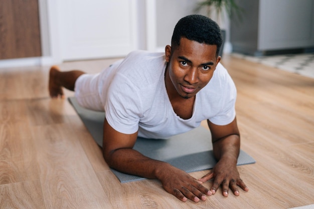 Vista aproximada do homem afro-americano exercitando-se em posição de prancha no chão durante o treino