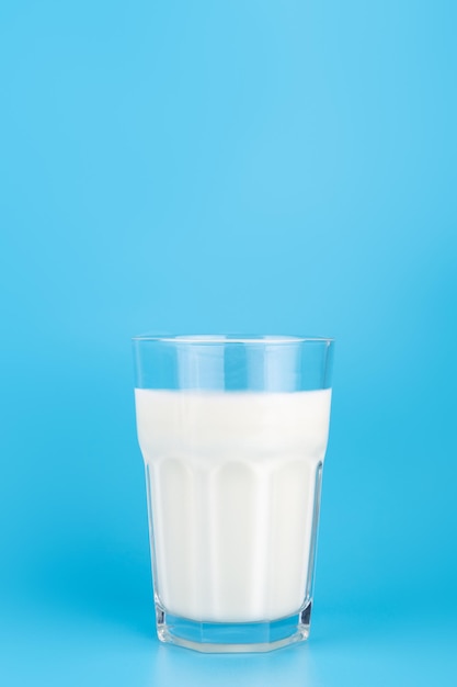 Vista aproximada do leite branco em vidro transparente facetado na vista lateral do fundo azul Produtos lácteos