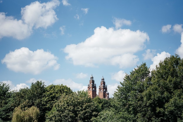 Una vista de árboles verdes contra el cielo azul con nubes blancas en el parque kelvingrove hacia mus kelvingrove