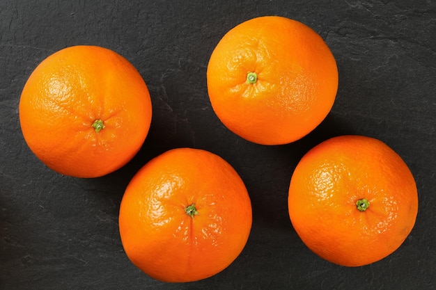 Vista de arriba hacia abajo, cuatro naranjas enteras en pizarra negra.