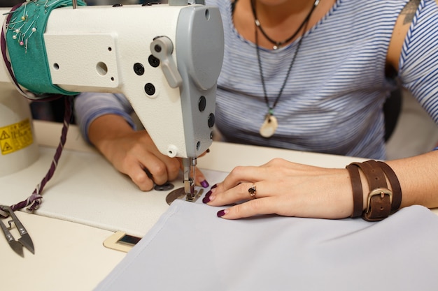 Vista desde arriba en manos del sastre femenino trabajando en la máquina de coser. industria de fabricación de vestidos