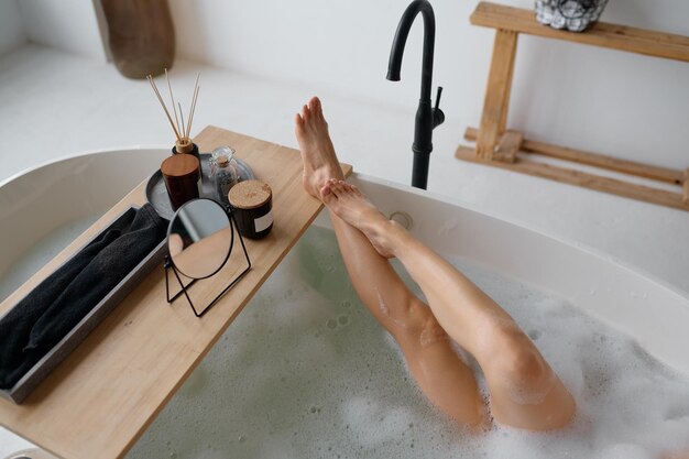 Vista desde arriba sobre la pierna femenina delgada mojada en un baño espumoso. Spa de día en casa, procedimiento de aroma en la bañera, descansar y refrescarse después del trabajo, momento para uno mismo