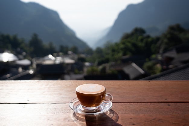 Vista del arte del latte de té con leche caliente en la mesa de madera con un paisaje relajante en la aldea de Pha Hee, Chiang Rai, Tailandia