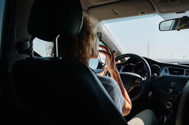 Vista del asiento trasero de ángulo bajo de una mujer que conducía su coche. Ella se toca los labios.