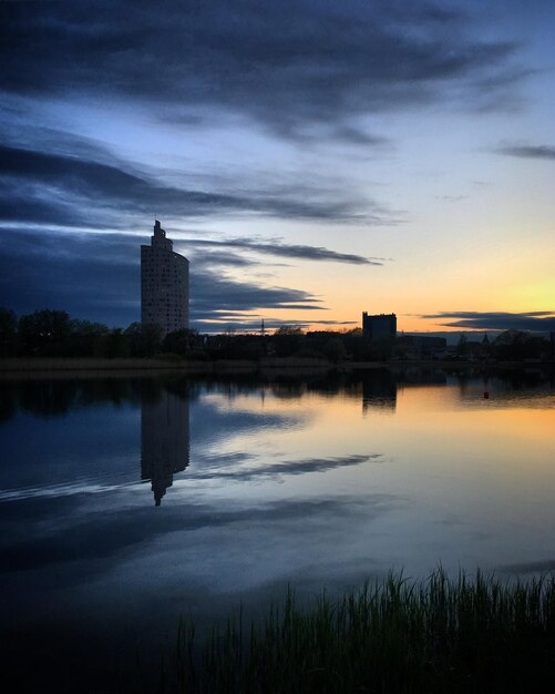 Una vista del atardecer de un edificio y un lago con una torre al fondo.