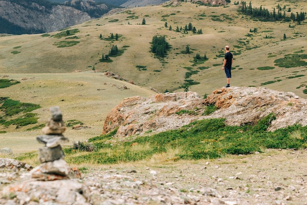 Vista atmosférica de um homem de pé sobre uma rocha e olhando para longe contra o pano de fundo de um vale de montanha