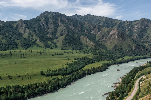 Vista atmosférica del valle verde de la montaña con el camino a lo largo del río turquesa