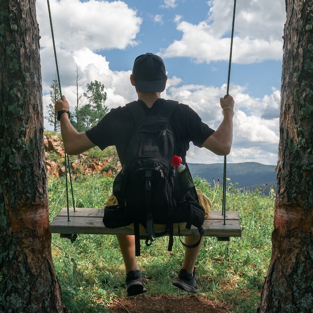 Vista desde atrás de un chico joven con una gorra en un columpio sobre un fondo de nubes.