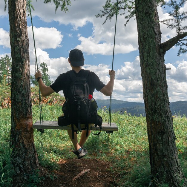 Vista desde atrás de un chico joven con una gorra en un columpio sobre un fondo de nubes.