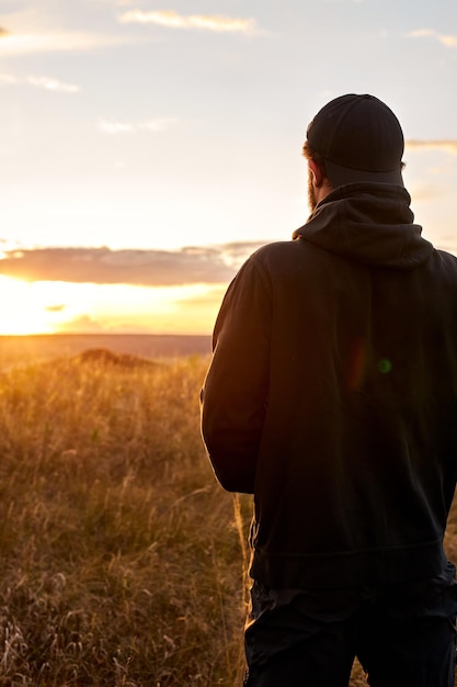 Vista desde atrás de un hombre irreconocible mirando la puesta de sol, en contemplación. vista trasera. pensamiento masculino joven, después del entrenamiento deportivo al aire libre. concepto de estilo de vida de las personas