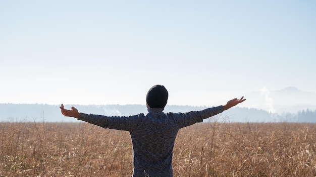 Vista desde atrás de un joven parado en la naturaleza con los brazos extendidos disfrutando y celebrando la vida