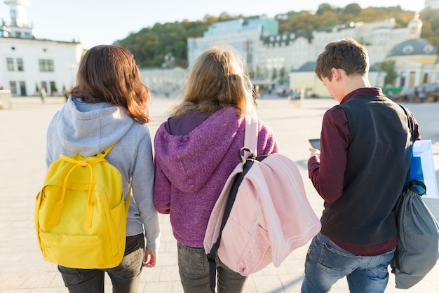 Vista desde atrás de tres estudiantes de secundaria con mochilas