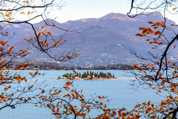 Vista através dos galhos de árvores de outono na pequena Ilha dos Coelhos, no lago de Garda