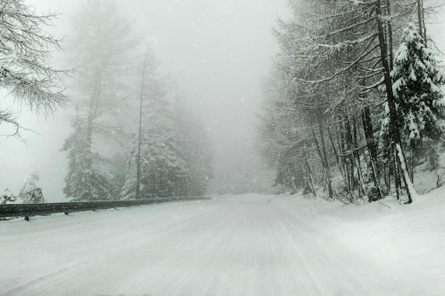 Vista desde un automóvil que viaja a través del invierno cubierto de nieve, fuertes nevadas, poca visibilidad, niebla y neblina a distancia: condiciones de conducción peligrosas.