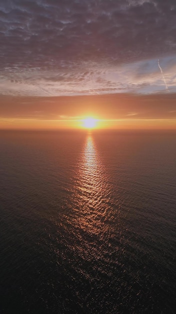 Una vista desde un avión no tripulado volando sobre el mar temprano en la mañana al amanecer con el sol naciente y un cielo colorido