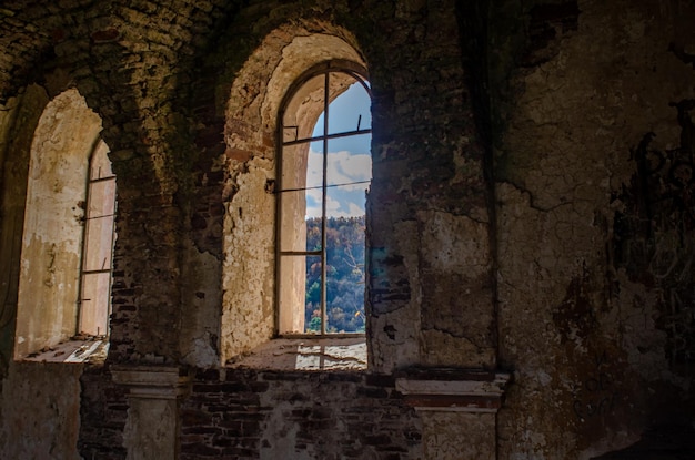 Vista del bosque bajo el cielo azul a través de las ventanas de la antigua iglesia en ruinas