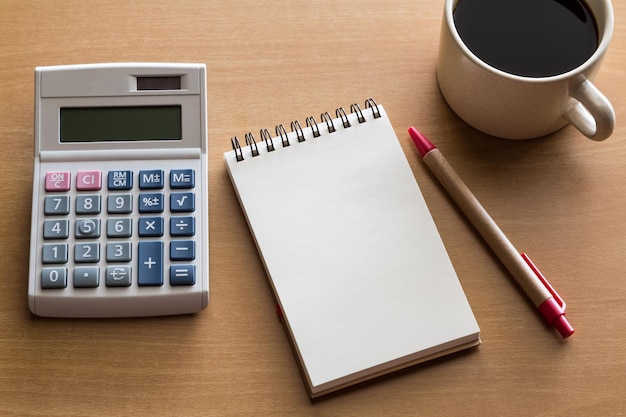 Vista de la calculadora con el bloc de notas por pluma y café negro en la mesa de madera
