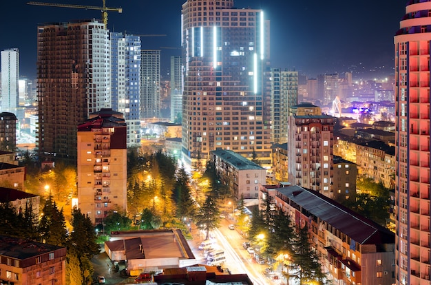 Vista de las calles de la ciudad nocturna de batumi con rascacielos, luz de las ventanas de los edificios de apartamentos, tráfico de automóviles en la carretera. vida urbana.