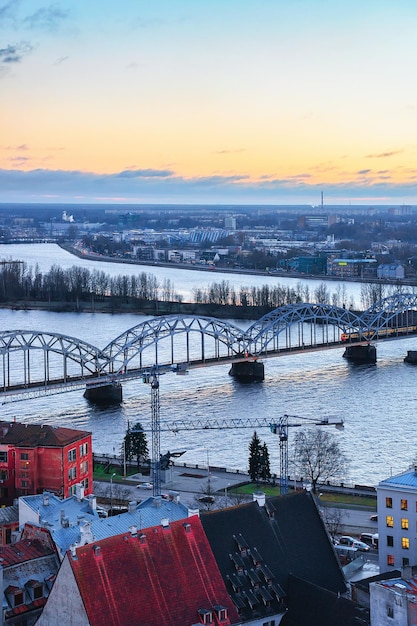 Vista del casco antiguo de Riga y el puente ferroviario sobre el río Daugava al atardecer en invierno