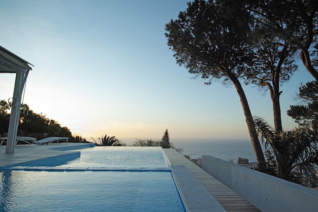 Vista cênica do pôr do sol de uma piscina infinita com um oceano de fundo do oceano Piscina ao ar livre de luxo em um terraço no terraço de um hotel de condomínio à noite Horizonte de céu azul com copyspace