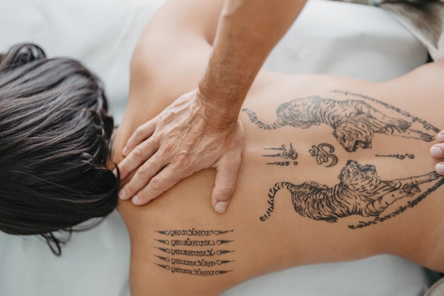 Vista cenital de la mano de un masajista presionando la parte superior de la espalda tatuada de una mujer