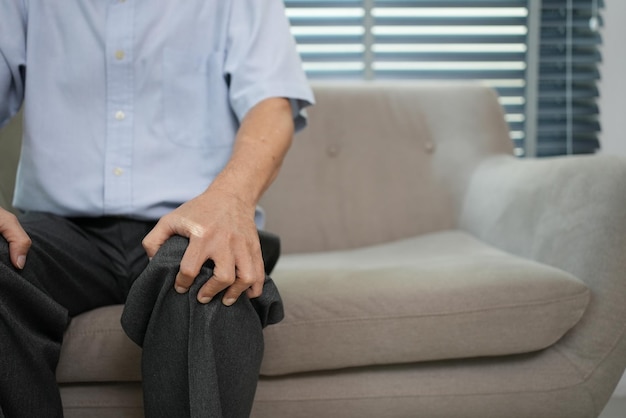 Vista de cerca del abuelo mayor que sufre de dolor de rodilla sentado en el sofá