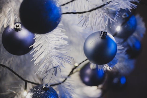 Vista de cerca de adornos navideños azules colgando del árbol de navidad blanco