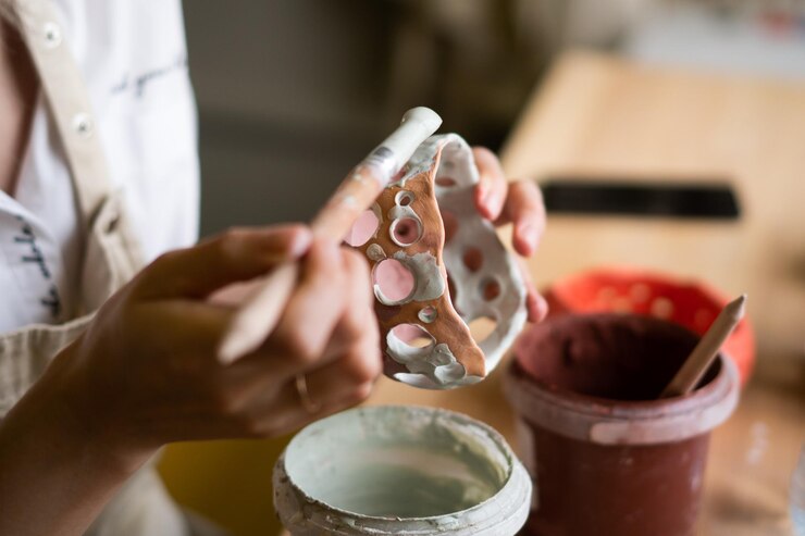 Foto vista de cerca de una alfarera que usa un delantal usando un pincel de esmalte para pintar en la olla