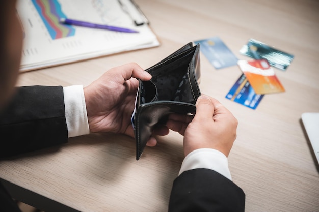 Vista de cerca de ángulo alto de manos de un empresario en ropa formal mirando una billetera vacía con tarjetas e informe financiero en la mesa