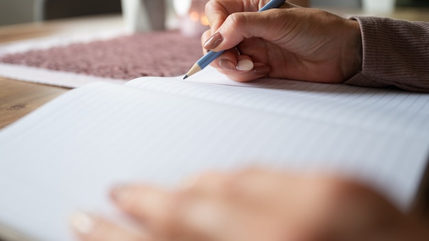 Vista de cerca de ángulo bajo de manos femeninas escribiendo en el cuaderno en casa.