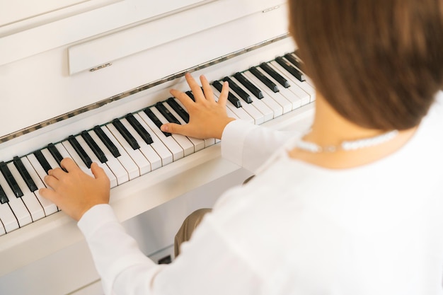 Vista de cerca desde atrás de una pianista irreconocible tocando un piano clásico en casa disfrutando de música virtuosa en el tiempo libre