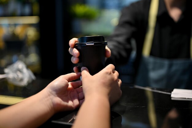 Vista de cerca del barista masculino entregando una taza de café para el cliente