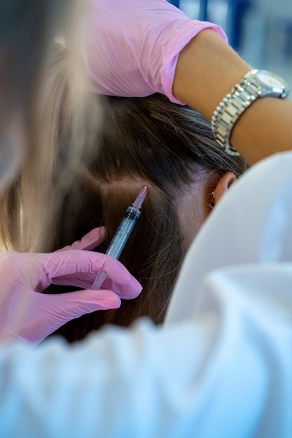 Vista de cerca de la cabeza de la mujer y las manos de los médicos con jeringa procedimientos profesionales de mesoterapia inyecciones de vitaminas en el área del cabello