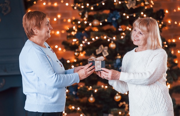 Foto vista de cerca de la caja de navidad por dos ancianas en la habitación decorada de navidad.